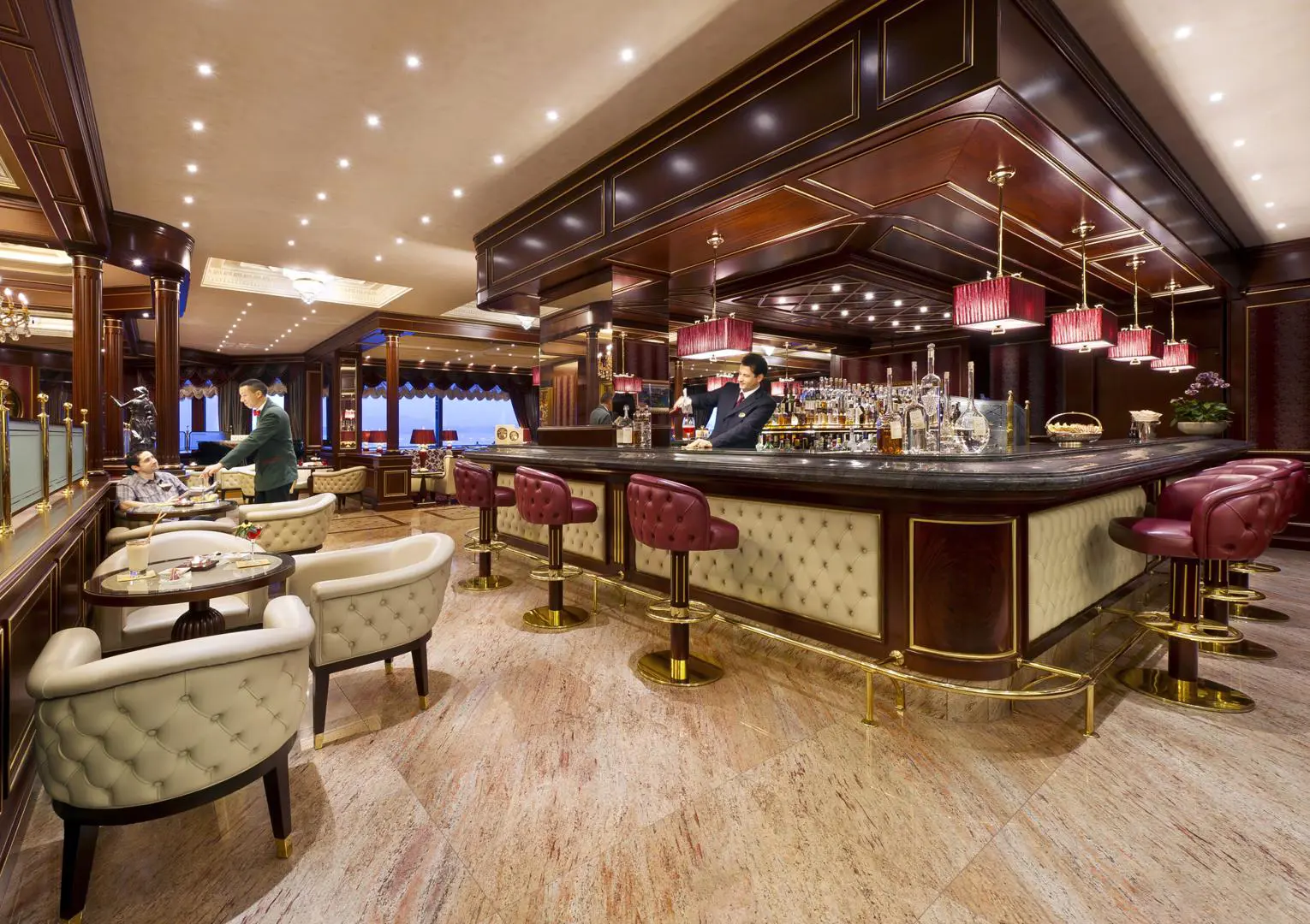 Bar area at Grand Hotel Dino in Baveno featuring deep red and neutral tones, with a dark wood bar and a bartender pouring a drink