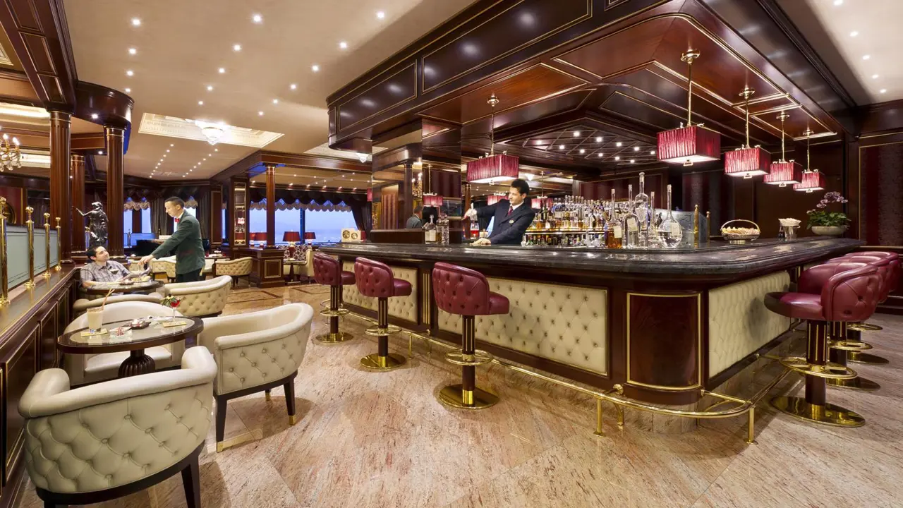 Bar area at Grand Hotel Dino in Baveno featuring deep red and neutral tones, with a dark wood bar and a bartender pouring a drink