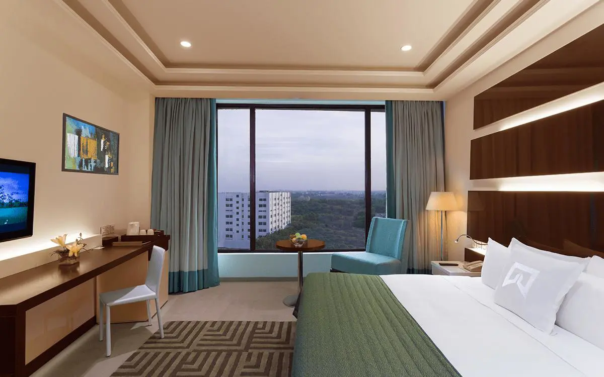Modern room at WelcomHotel by ITC in Dwarka with a large bed, work desk and city view through wide windows