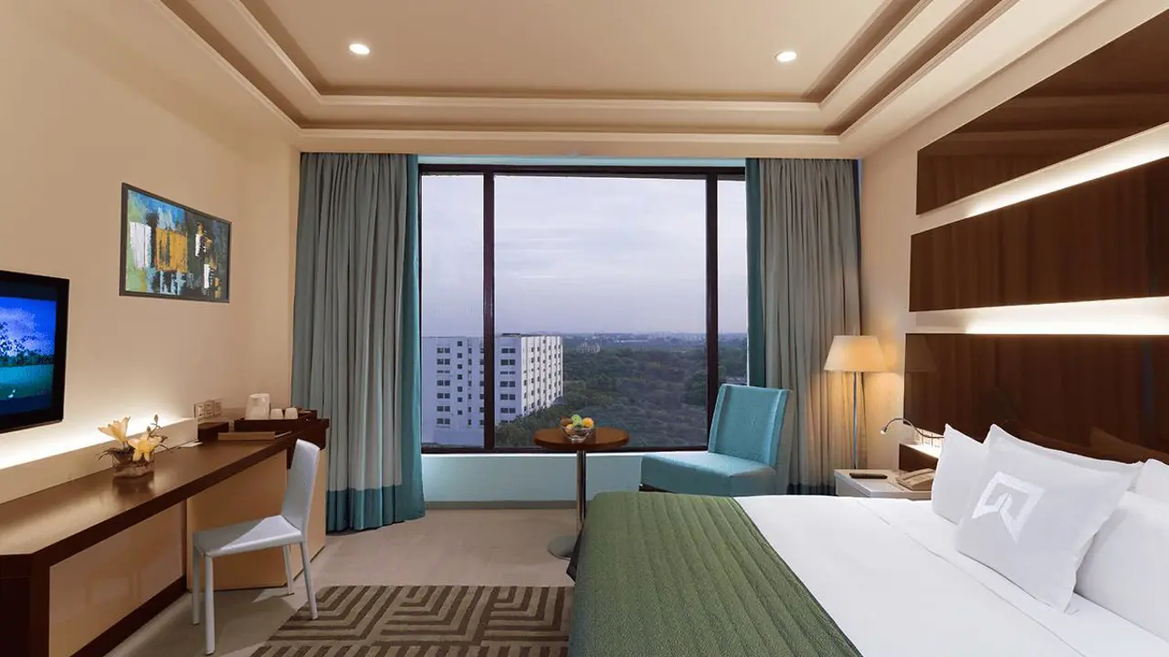 Modern room at WelcomHotel by ITC in Dwarka with a large bed, work desk and city view through wide windows