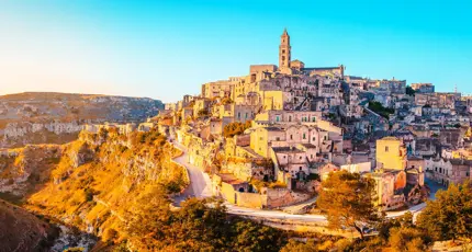 A panoramic view of the historic stone town of Matera, Italy, with ancient buildings stacked on a hillside in the golden glow of sunset