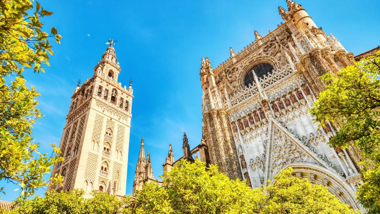 Looking up at Seville Cathedral in Spain on a sunny day, showcasing its detailed Gothic architecture against a clear blue sky
