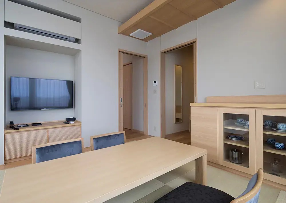 Stylish and spacious corner deluxe room in Hotel Kowakuen Haruka, with minimalist Japanese décor, featuring a low wooden table, tatami flooring, and display cabinets with tableware