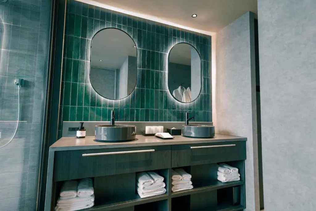 Modern bathoom at FAV LUX Nagasaki with double sinks, green tiled wall, round mirrors, and neatly arranged towels