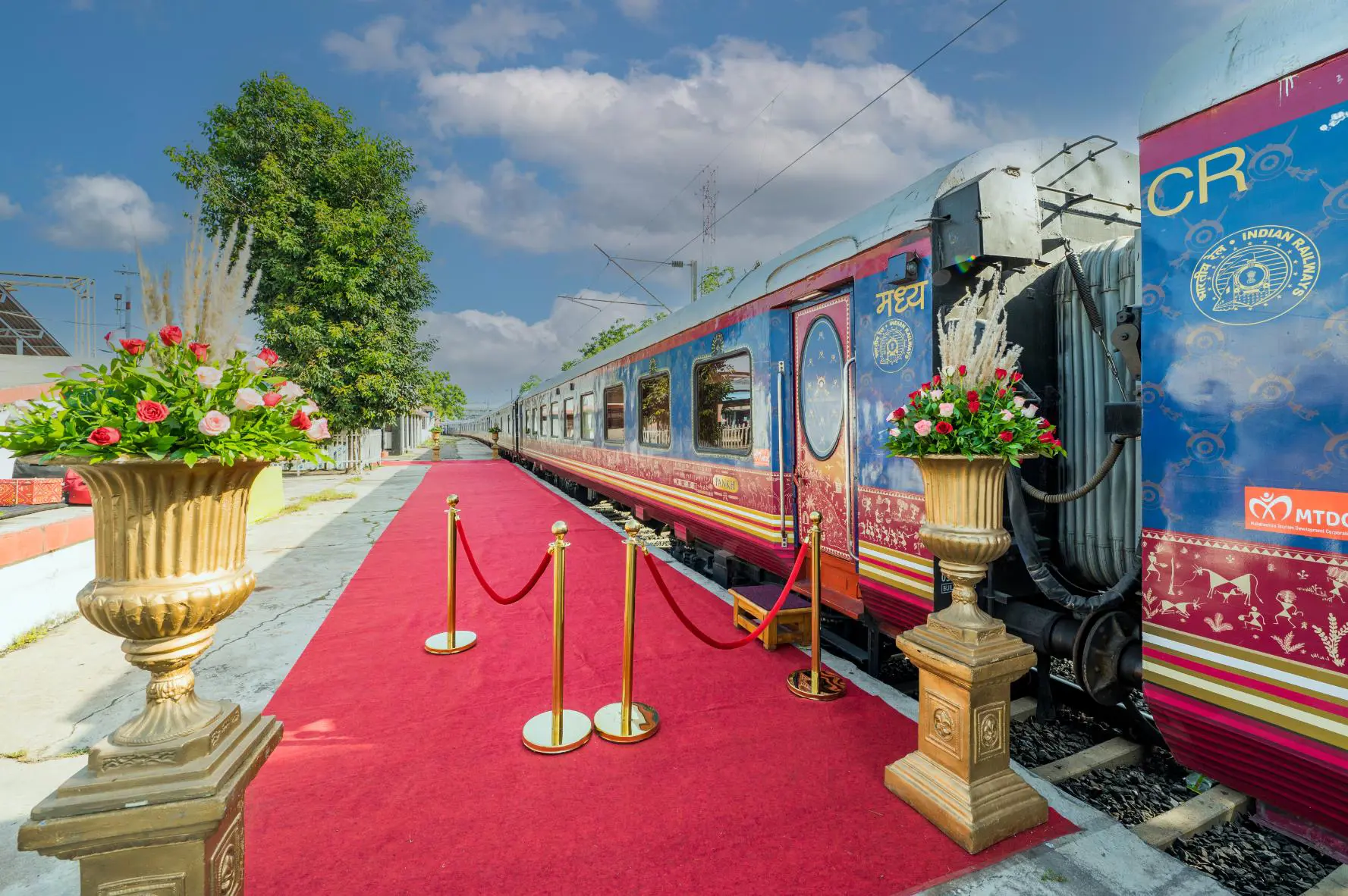 Exterior view of the Deccan Odyssey train at the platform, with a red carpet and gold barriers by the entrance