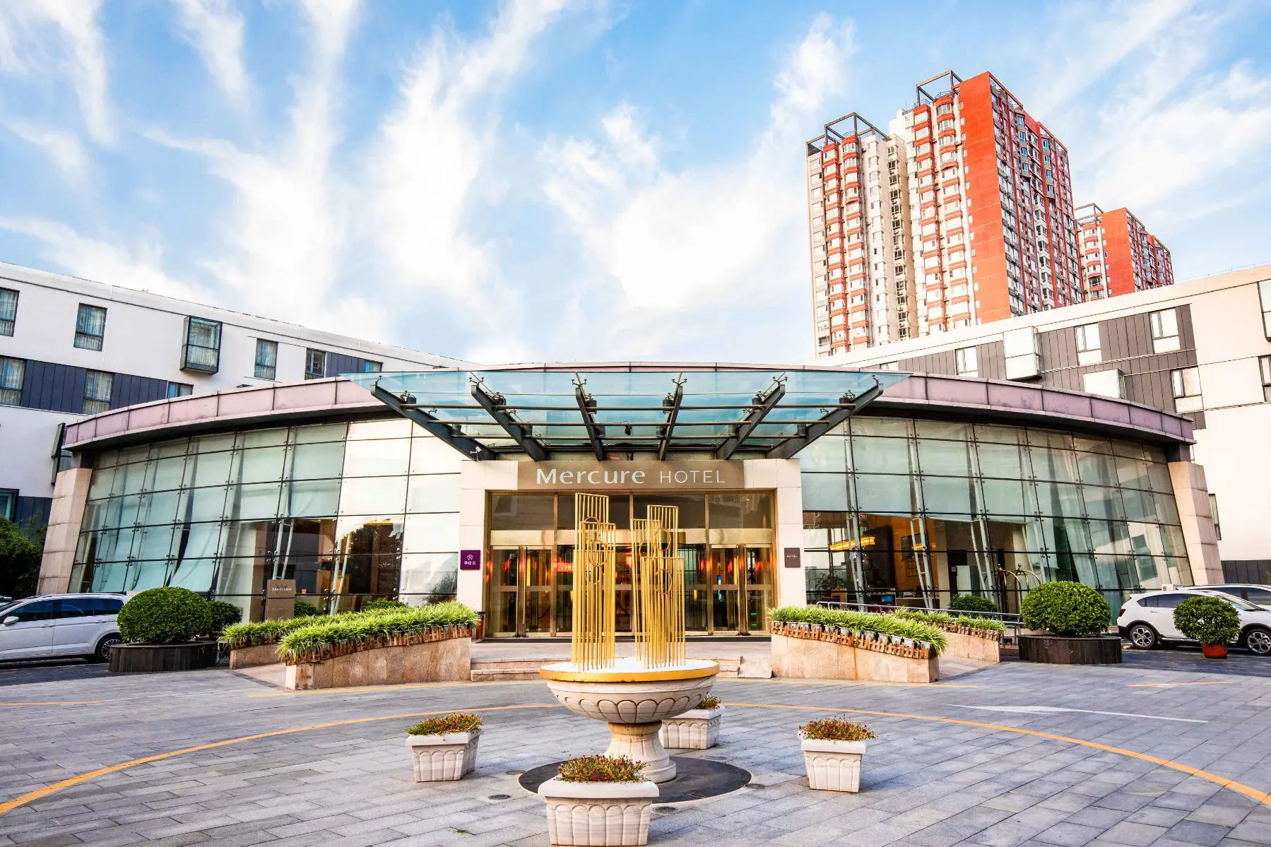 Exterior view of the Mercure Beijing Downtown hotel with a small fountain and potted plants in front of the modern glass entrance in Beijing, China