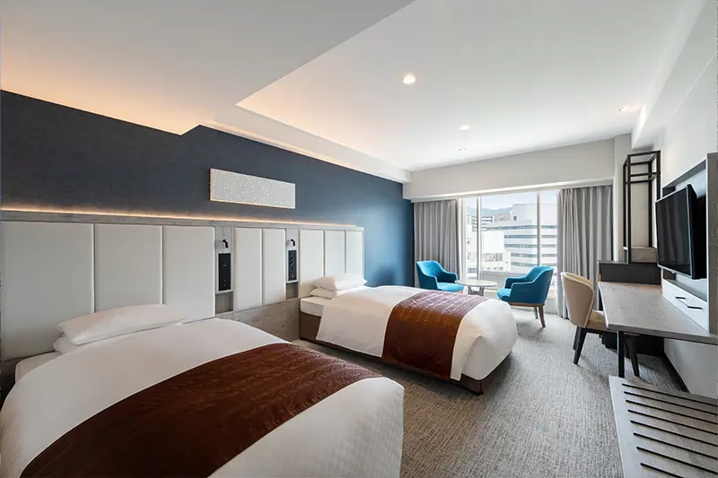 Contemporary twin room at Hotel New Nagasaki with two single beds, a dark accent wall, and city view through large windows