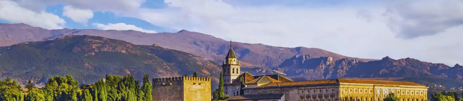 Panoramic view of the Alhambra Palace in Spain on a sunny day, with its historic architecture set against a backdrop of rolling hills and a bright blue sky