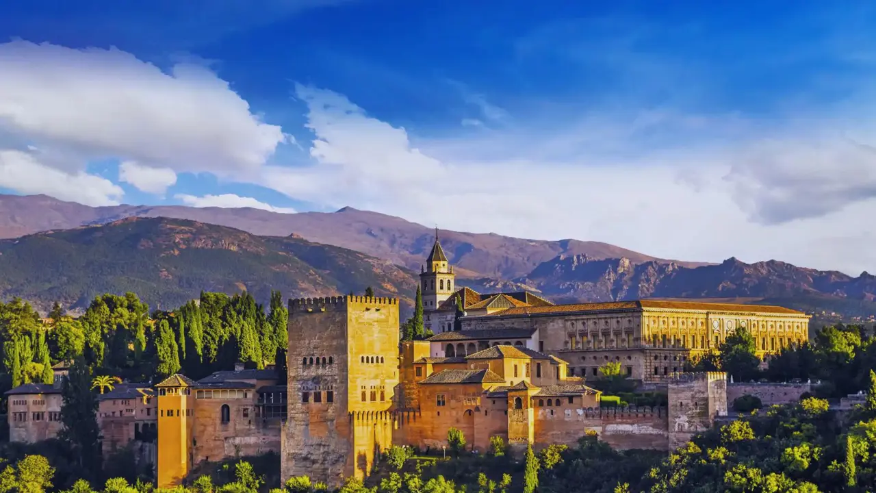 Panoramic view of the Alhambra Palace in Spain on a sunny day, with its historic architecture set against a backdrop of rolling hills and a bright blue sky