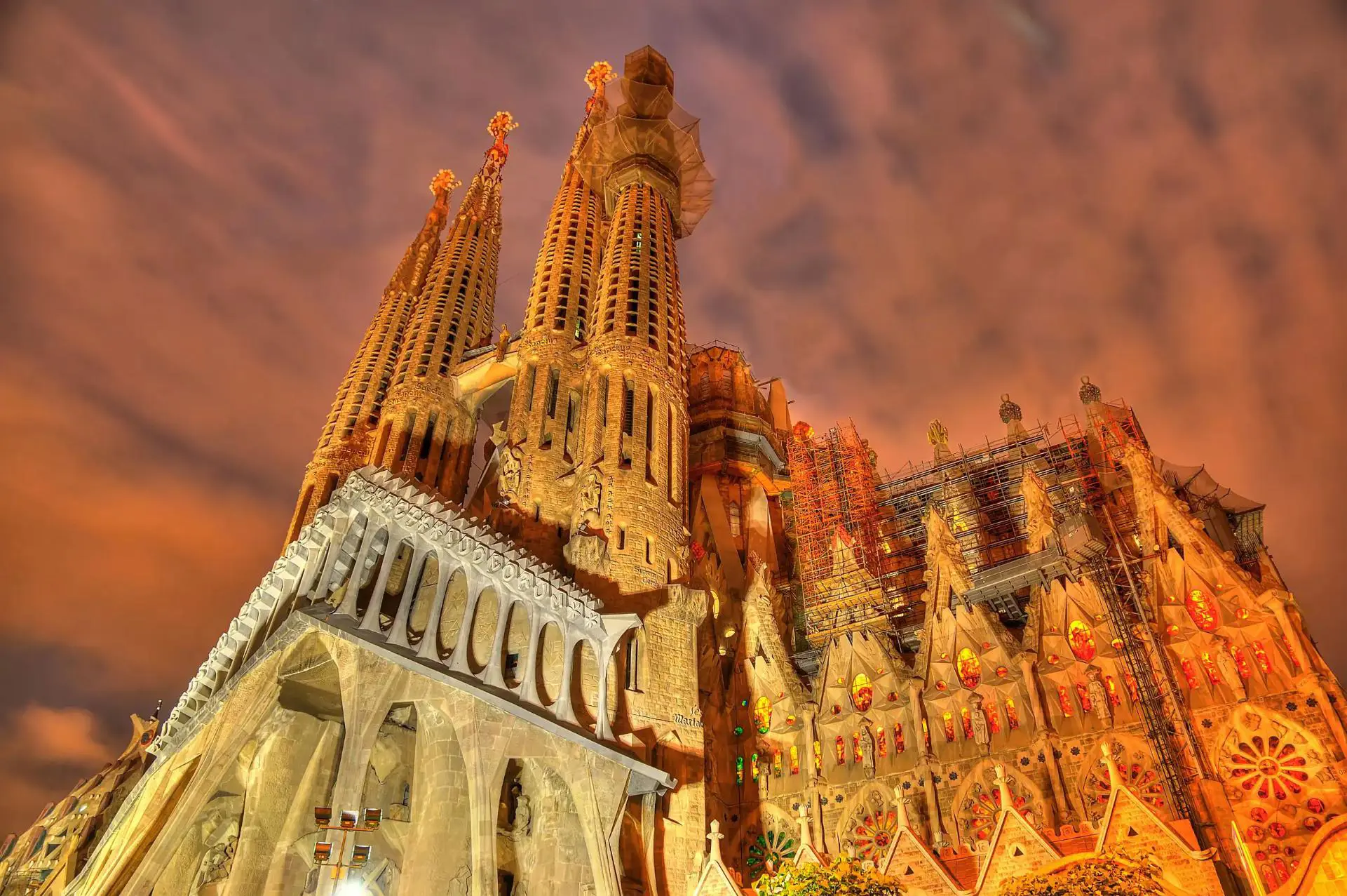 Night view of the illuminated Sagrada Família basilica in Barcelona, Spain, showcasing its intricate architecture and towering spires against a dramatic, cloudy sky