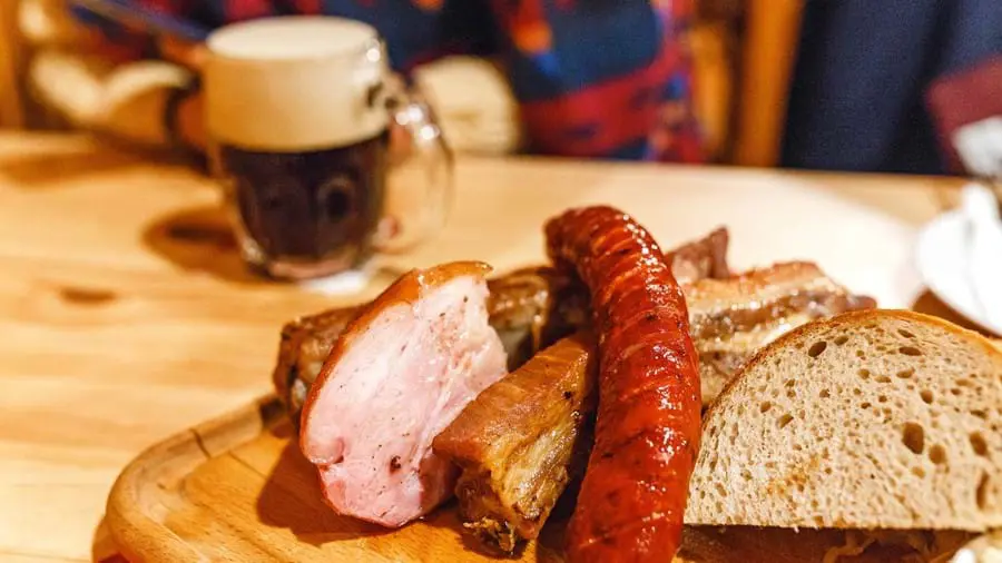 Close up of a plate of traditional sausage, pork meat and slices of bread.  Crafted Czech mug of beer in the background.