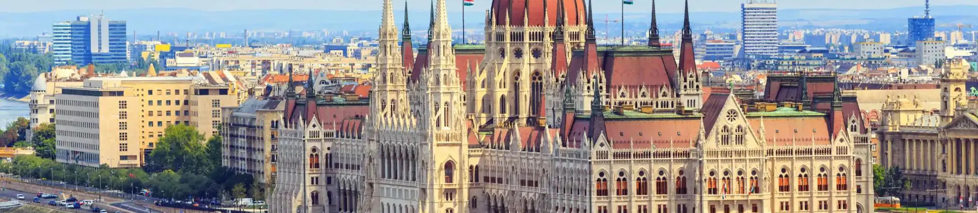 High angle shot of the Hungarian Parliament Building, with red roofs and spiky turrets and the Danube river in the left forefront