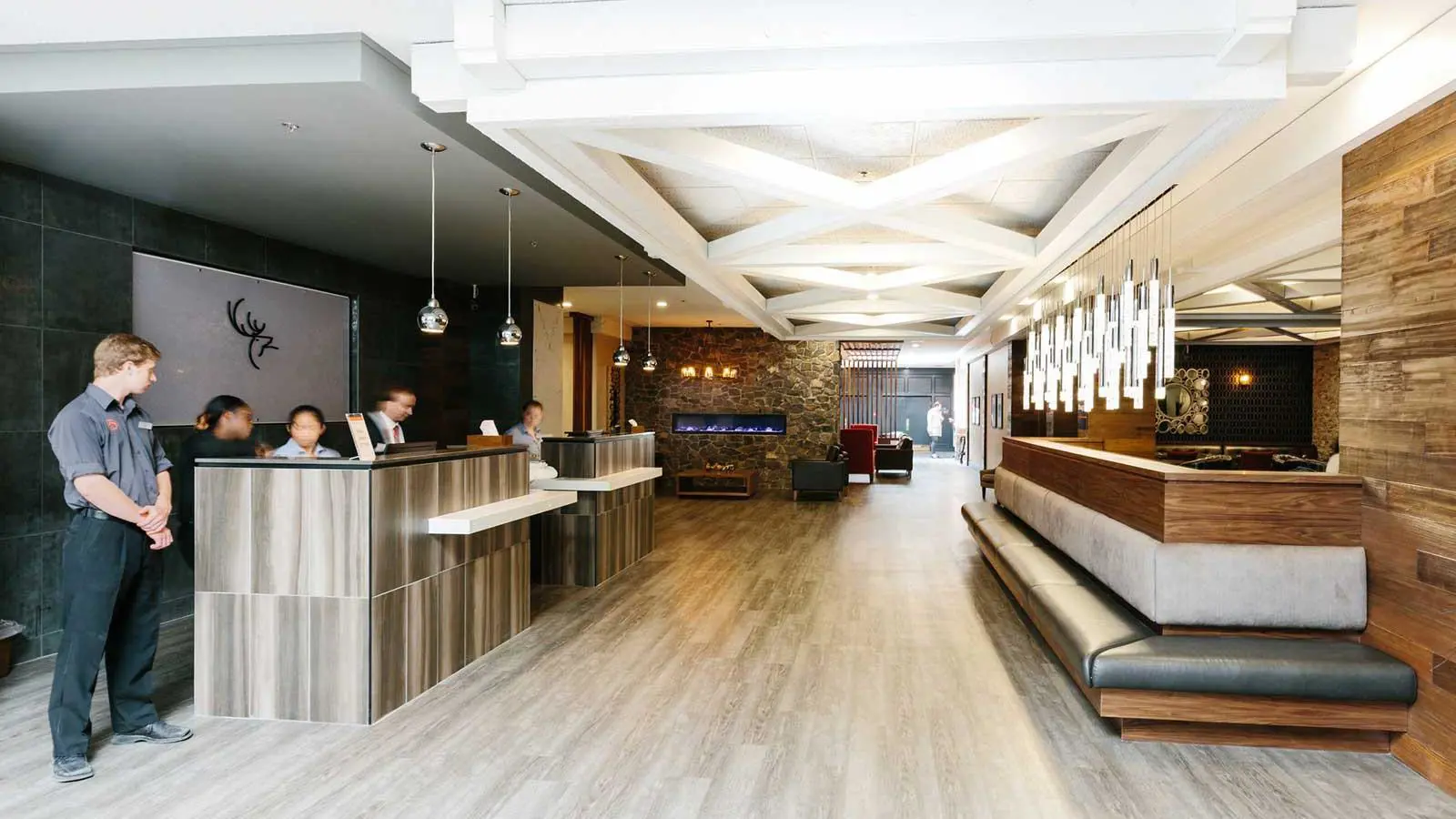 Modern hotel lobby at the Elk + Avenue with wood and stone accents, reception desks, hanging lights, and a lounge area with a fireplace