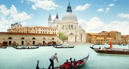 View of gondola boats travelling on the water and the Salute Church in Venice, Italy