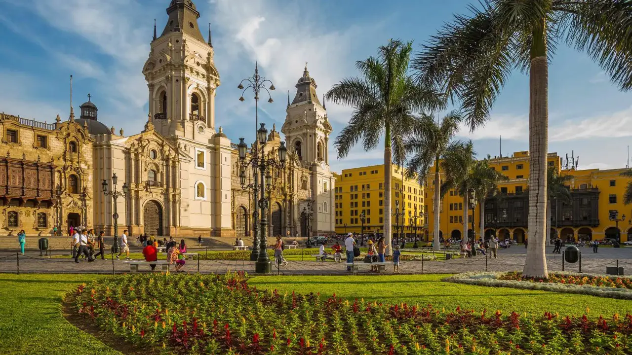 A view of the Cathedral of Lima in the Main Square of Lima, Peru, featuring colonial architecture, palm trees, and a sunny sky in the background