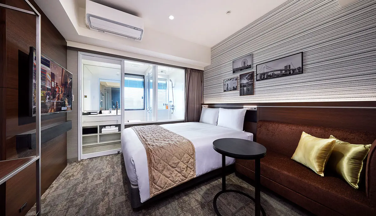 Double bedroom with an en-suite bathroom, decorated in warm brown and gold tones, featuring a large bed, elegant furnishings, and soft ambient lighting