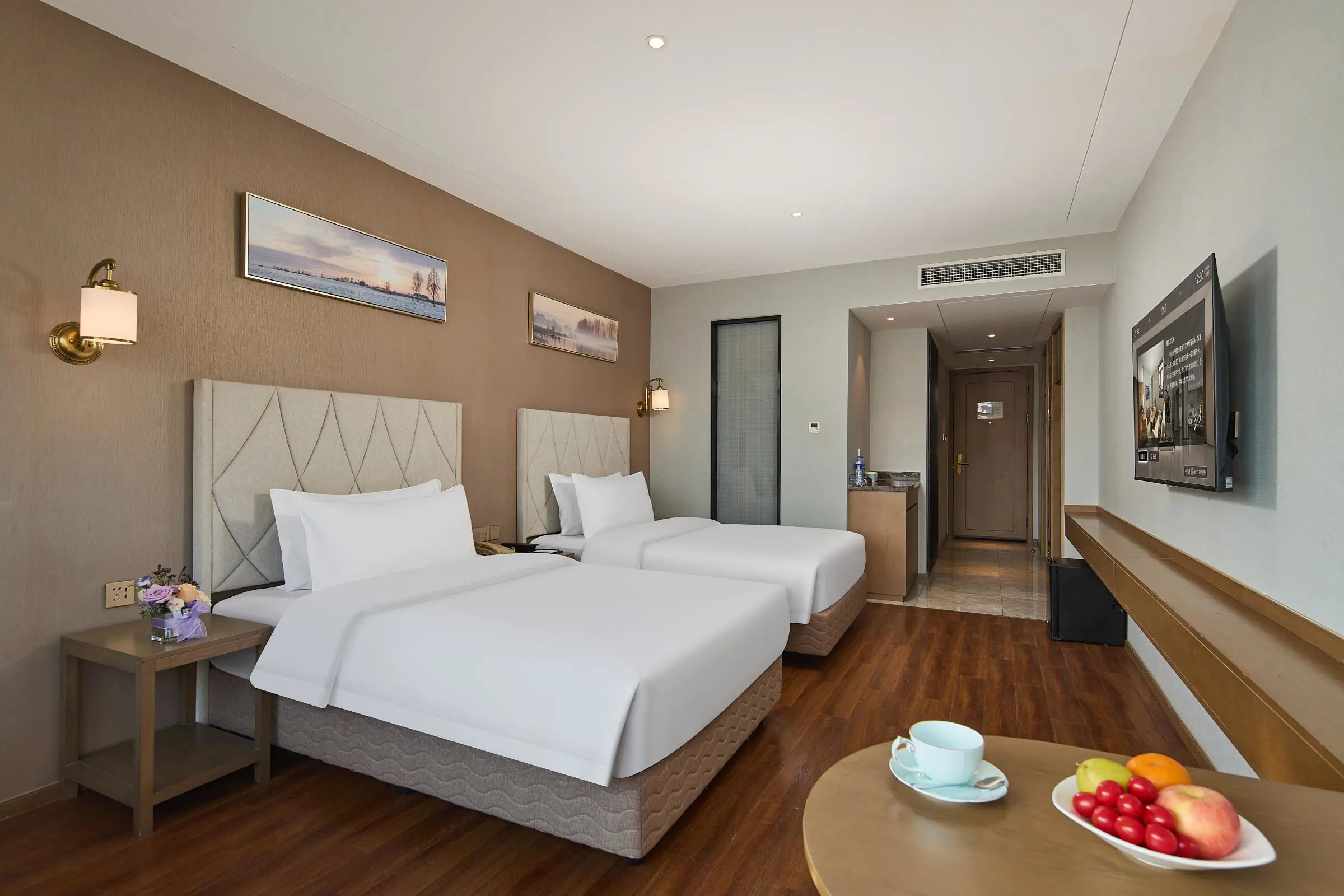 A contemporary hotel room at the Youngor Central Hotel in Suzhou, China, featuring two neatly made beds, a corner table with a fruit bowl, and a neutral yet inviting décor