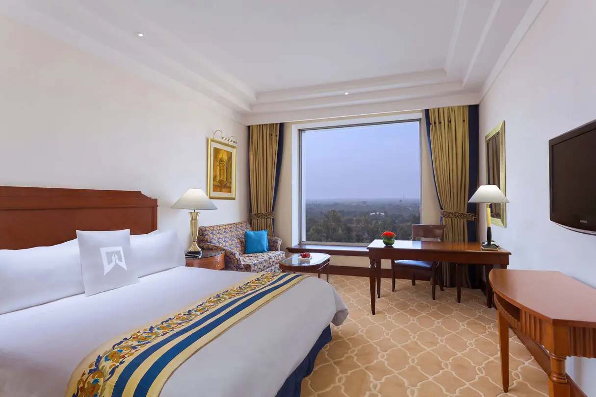 Elegant guest room at Sheraton New Delhi, featuring a king-sized bed, classic furnishings, large window with a city view, and warm, neutral décor