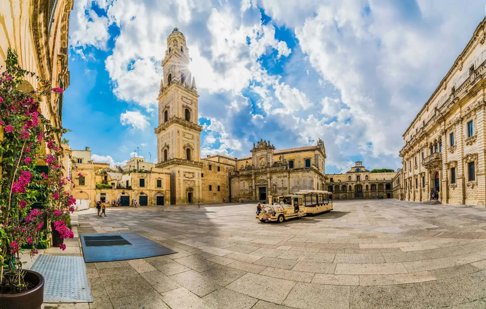 A square in Lecce, Italy, featuring a historic tower and a land train for tourists