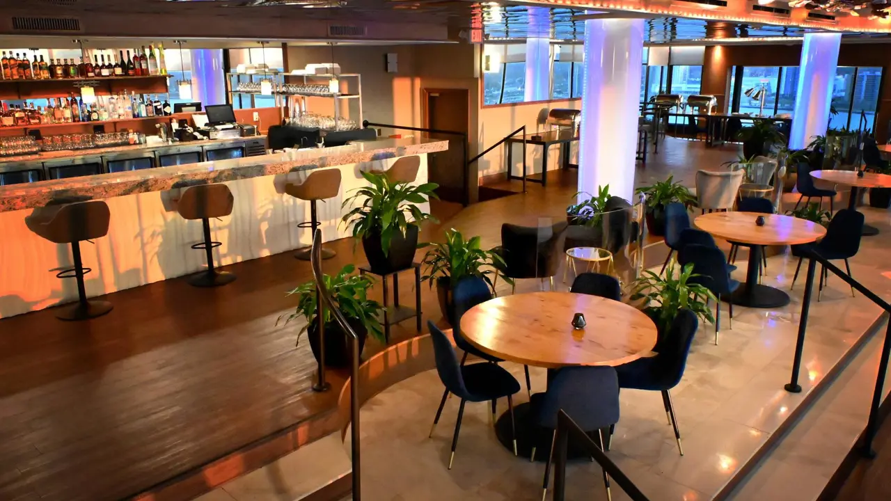 A stylish rooftop bar and restaurant at Fort Pontchartrain hotel with round tables, navy chairs, plants, and ambient lighting