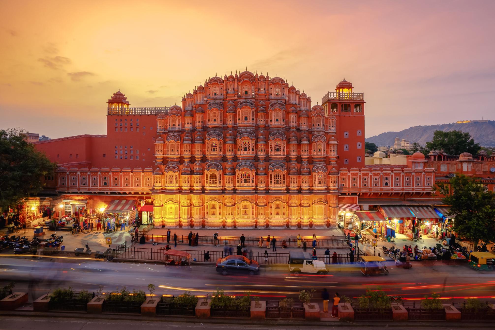 The Palace of the Winds in Jaipur illuminated at sunset, its ornate pink façade overlooking the street below