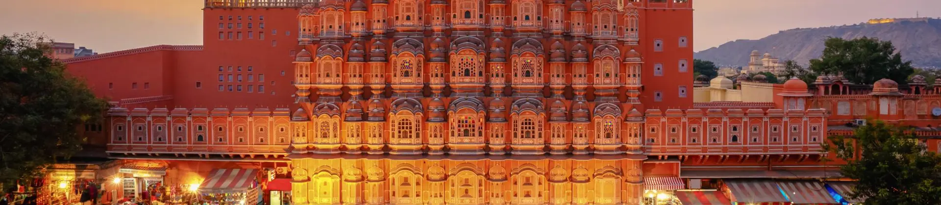 The Palace of the Winds in Jaipur illuminated at sunset, its ornate pink façade overlooking the street below