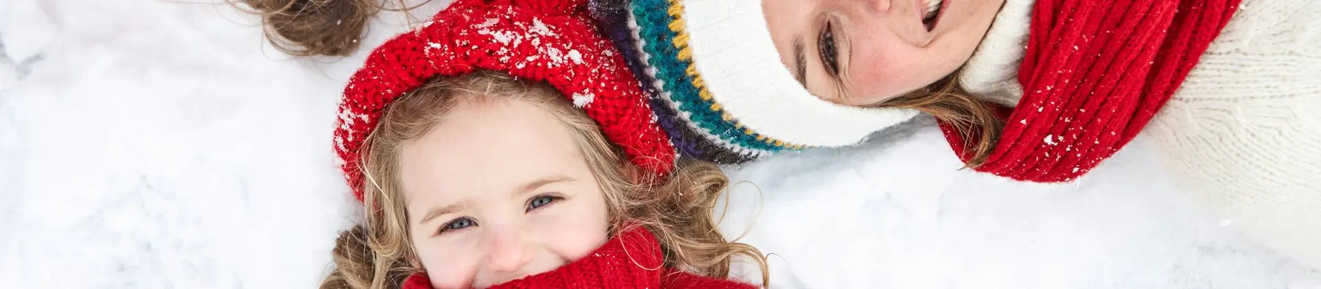 Face-shot of mother and two children lying in the snow, looking into the camera, laughing