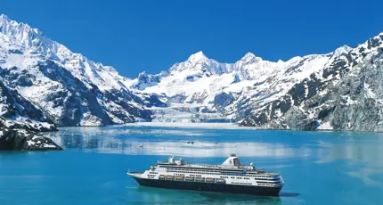 The MS Koningsdam cruise ship sailing through Glacier Bay, surrounded by calm icy waters and dramatic snow-capped mountains