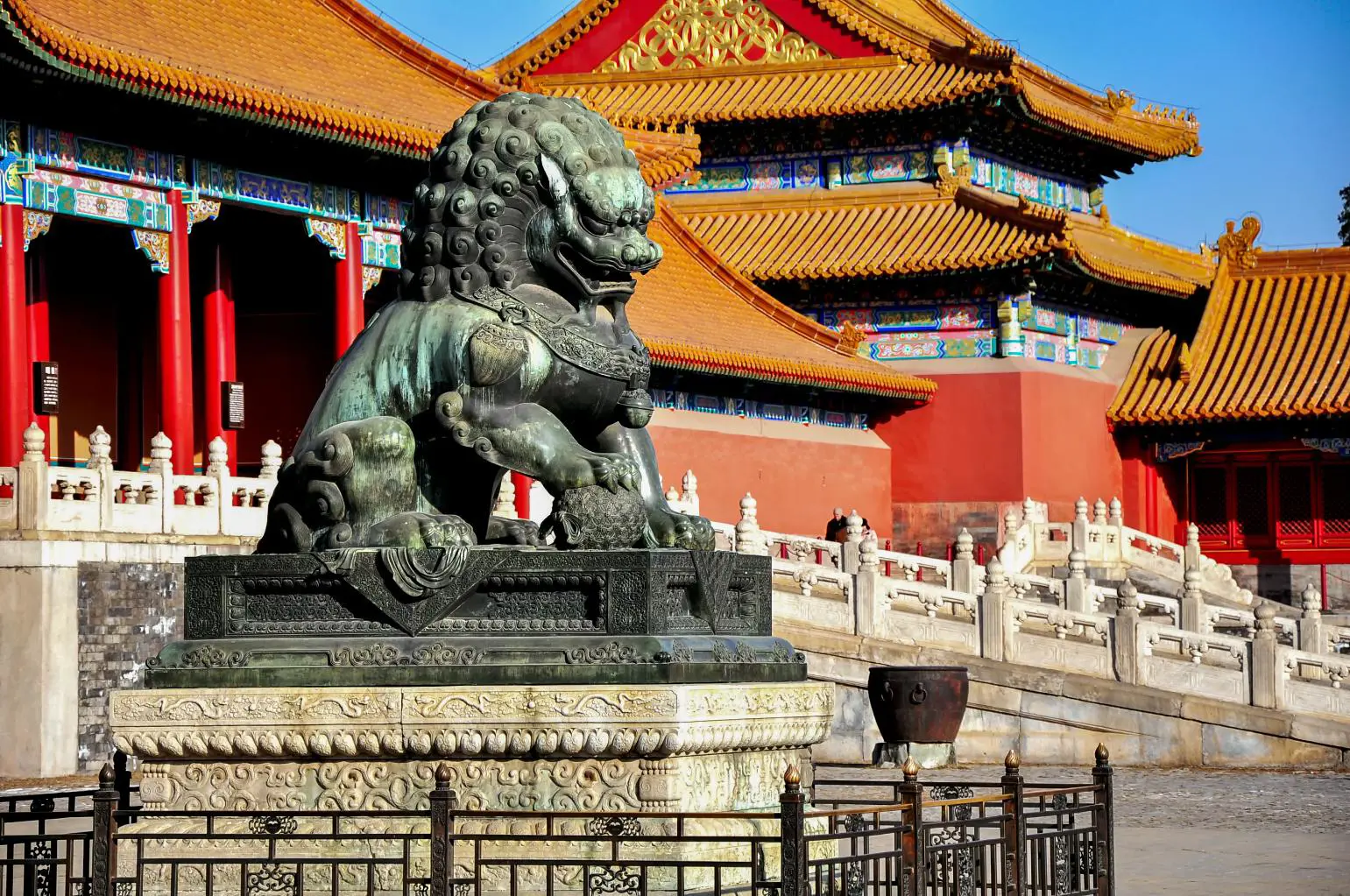 Detailed bronze lion statue before red and gold palace structures in the Forbidden City, Beijing, China