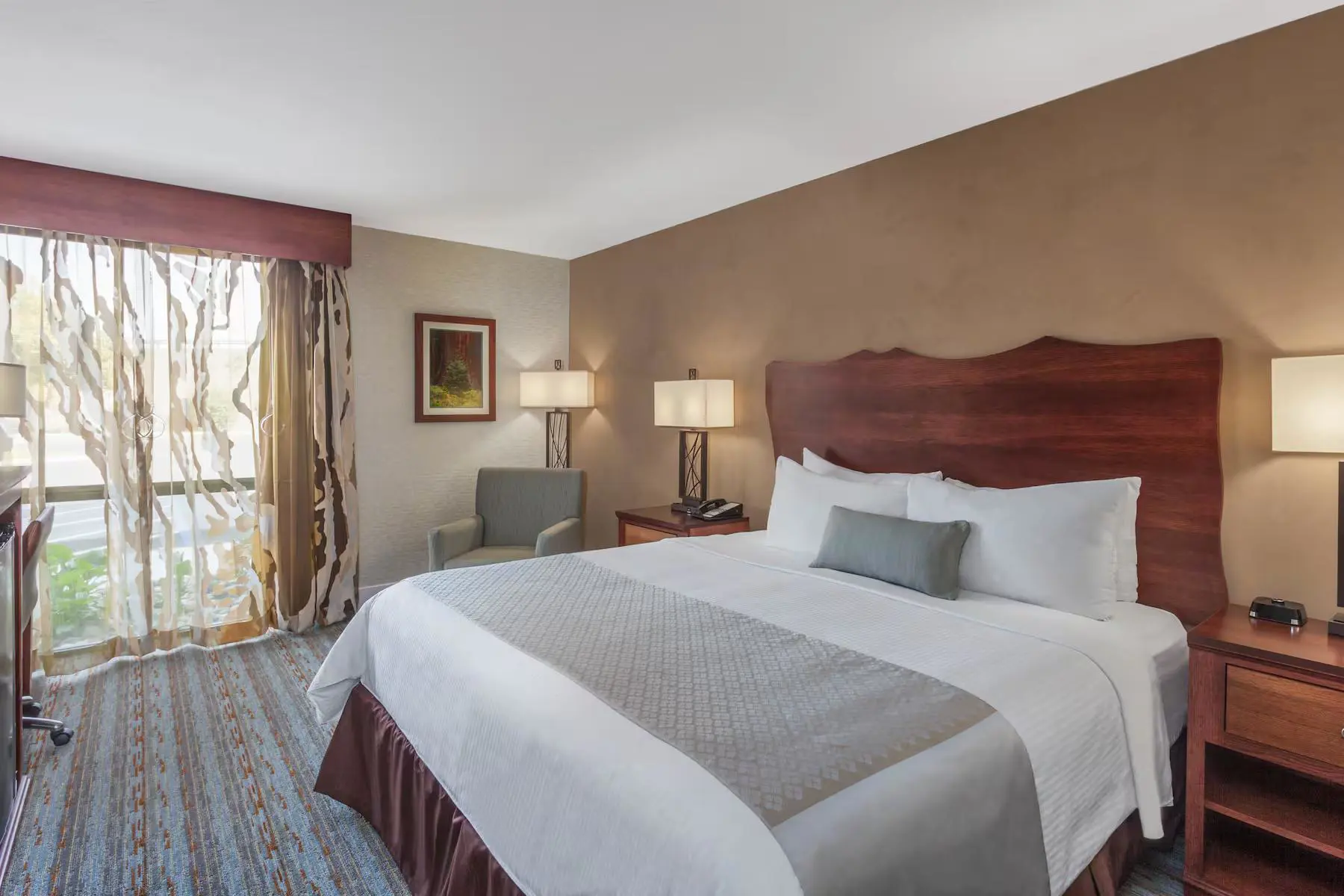 Spacious king bedroom at the Wyndham Hotel, Visalia, featuring a large bed with white linens, contemporary furnishings, and soft, warm lighting