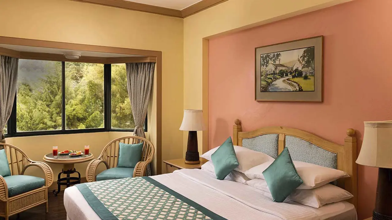 Deluxe room at Fortune Resort Sullivan Court in Ooty, with a cosy bed, pastel walls, and a bay window with a forest view