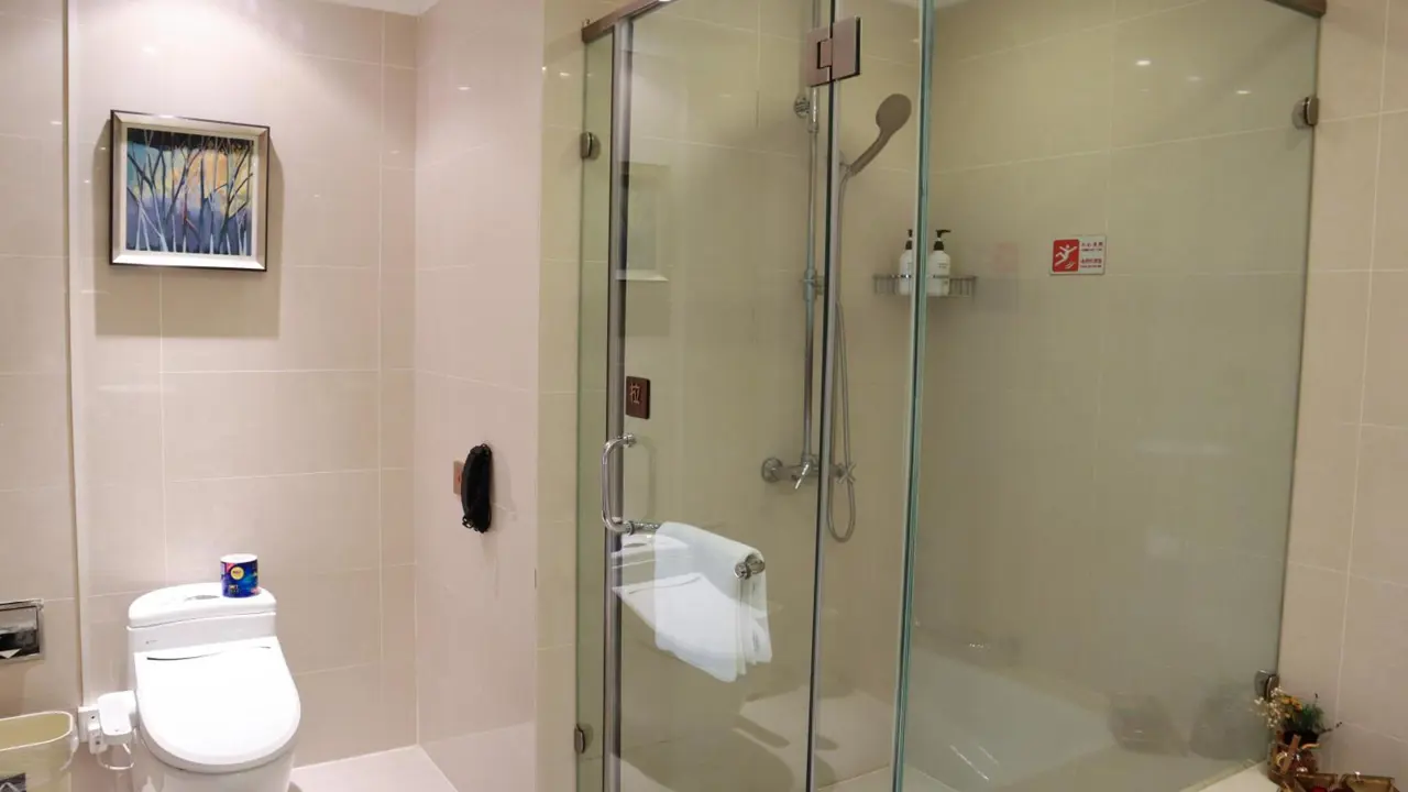 Modern bathroom with glass shower enclosure, toilet and wall art at the Shanghai Metropark Jichen Hotel in Shanghai, China