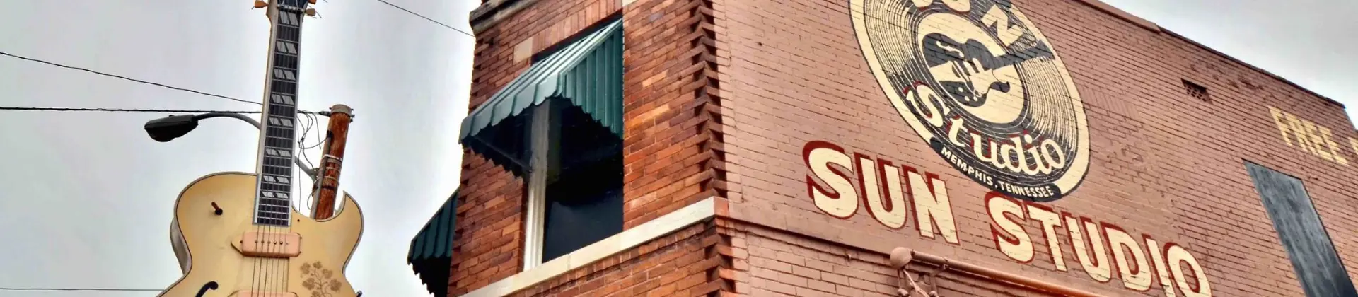 Sun Studio building with orange brick exterior, a large guitar-shaped sign outside, and the words “Sun Studio” painted in yellow on the side of the building