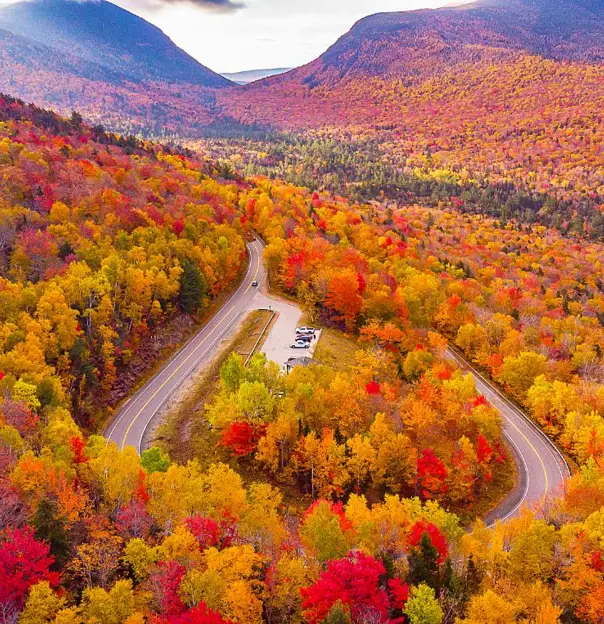 Kancamagus Highway in New Hampshire lined with vibrant autumn foliage, featuring a winding road surrounded by trees in shades of red, orange, and yellow