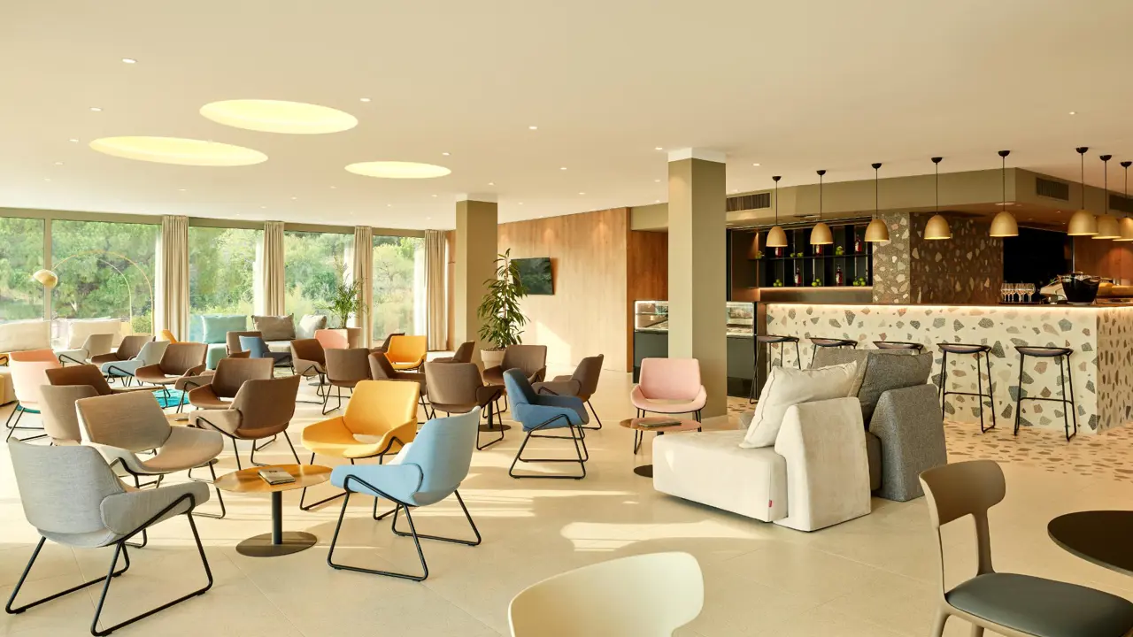 A stylish bar with large glass windows overlooking the green landscape. The bar at Hotel Horizont, Baška Voda features single seating, mini tables and lounge style seating