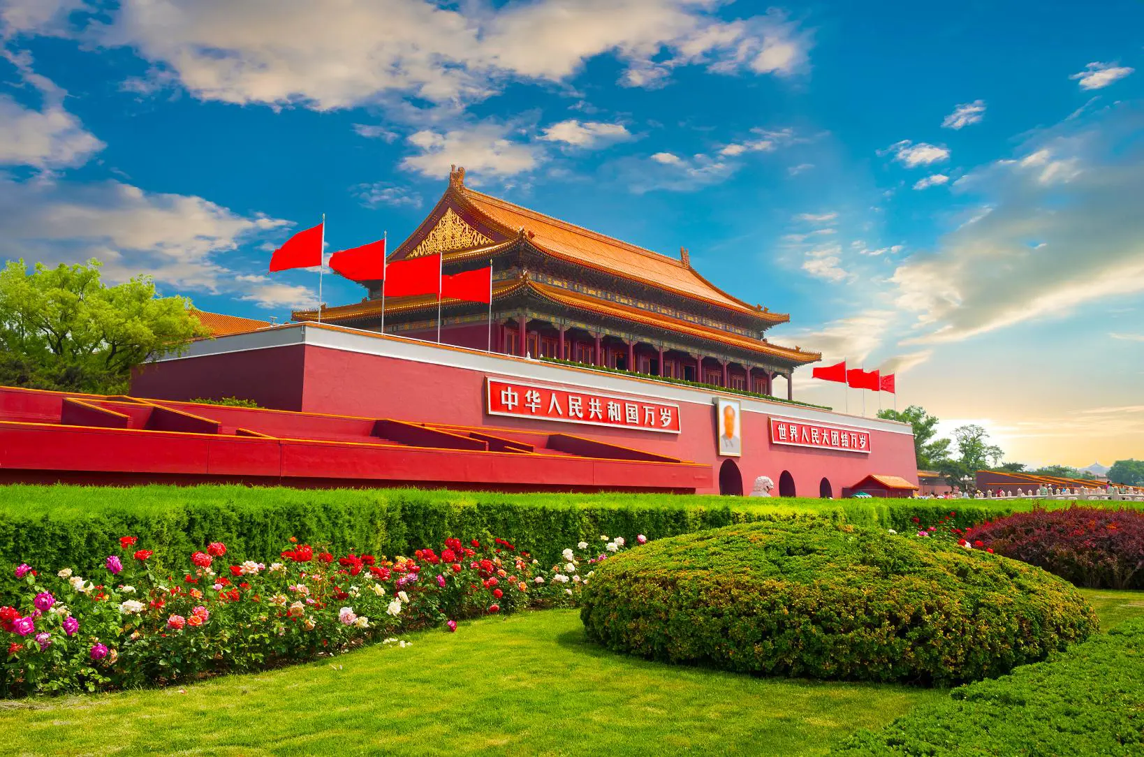 Tiananmen Gate with red flags and colourful gardens under a bright blue sky, Beijing, China
