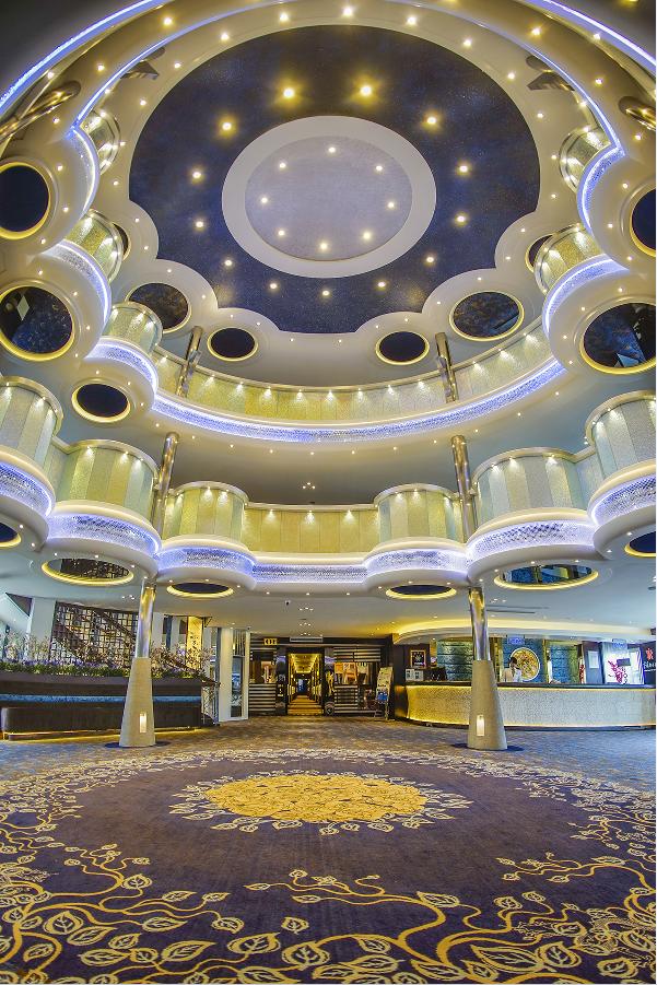 Grand lobby of a Victoria Cruises ship with a circular atrium, illuminated balconies and intricate carpet patterns creating a luxurious atmosphere