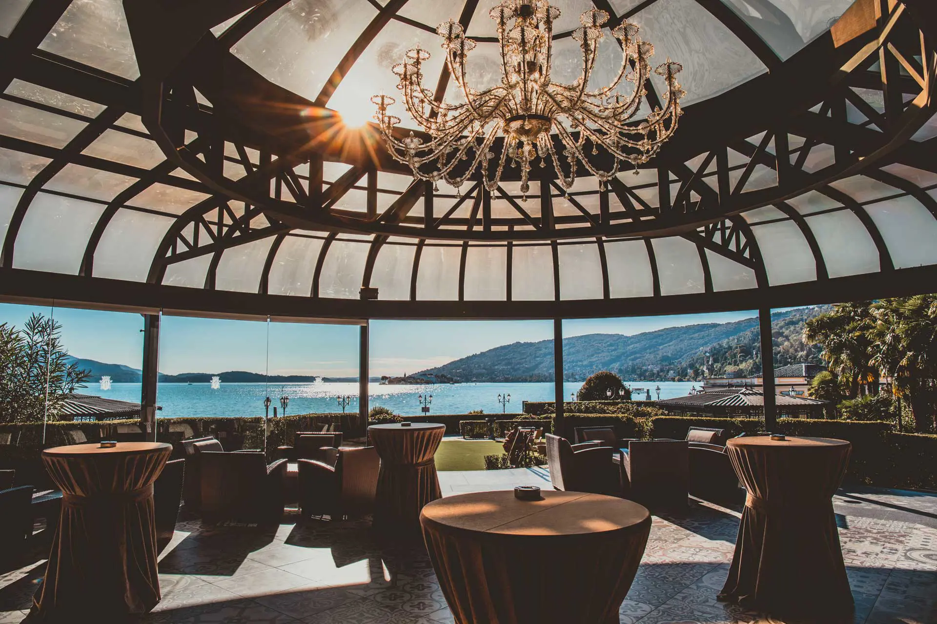 View from the restaurant at Grand Hotel Dino in Baveno, with a large panoramic window framing the lake and mountains, beneath a domed roof with a chandelier
