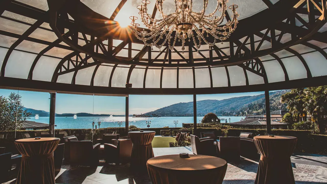 View from the restaurant at Grand Hotel Dino in Baveno, with a large panoramic window framing the lake and mountains, beneath a domed roof with a chandelier