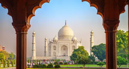 The Taj Mahal framed by an ornate archway, with green gardens in the foreground