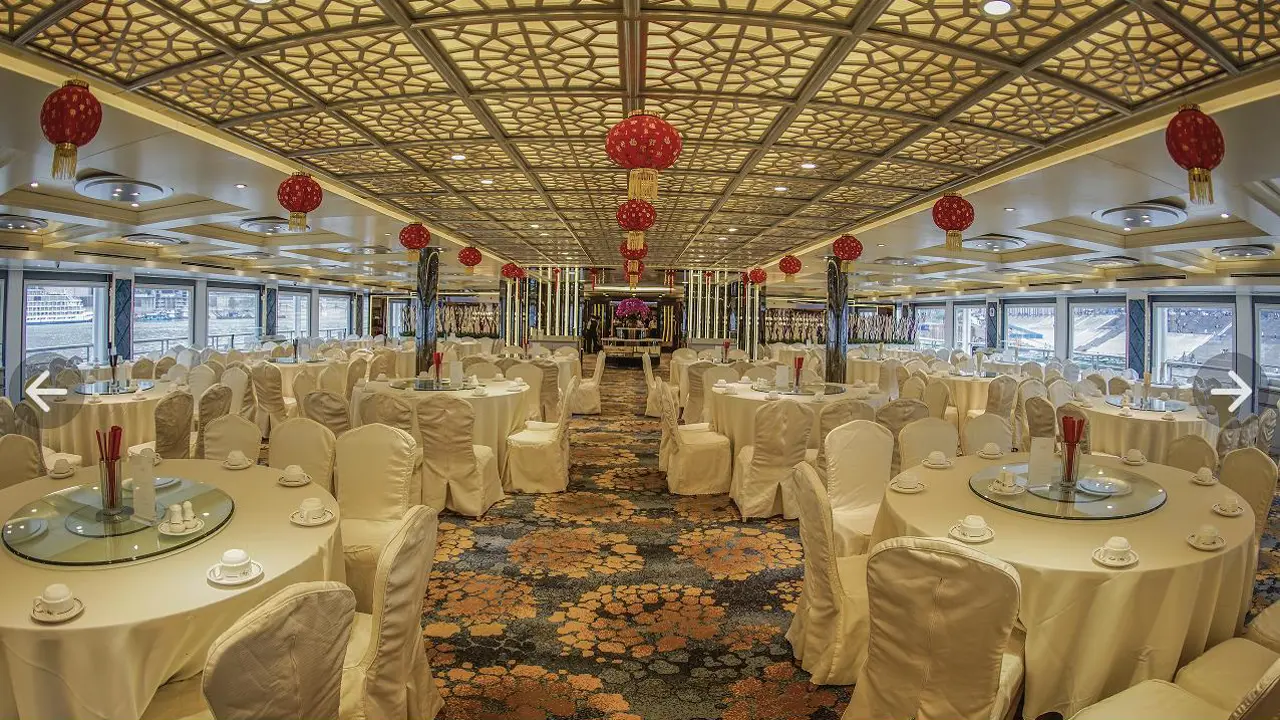 Elegant dining room aboard a Victoria Cruises ship, featuring round banquet tables with white linens, ornate ceiling panels and red lanterns for a traditional Chinese touch