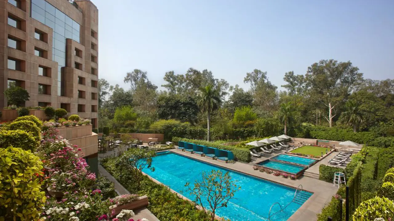 A view of the swimming pool and exterior of the Sheraton New Delhi, surrounded by landscaped gardens on a bright day