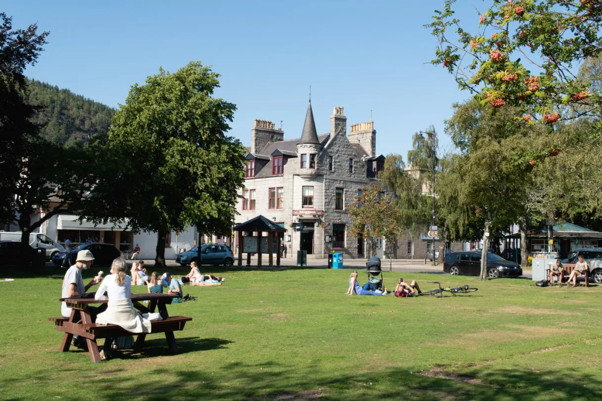 People enjoying sunny day and lying in the grass outside of the Glenmuick Church in the town centre of Ballater. Balmoral bar in the background.