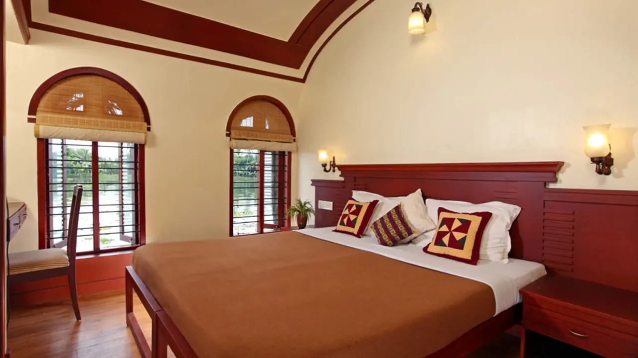 A cosy bedroom on a Keralan houseboat featuring rich wooden interiors and soft ambient lighting creating a warm, traditional feel