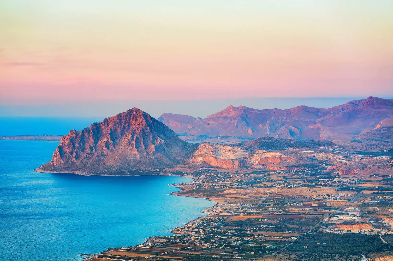 Mountain landscape of Erice, Sicily, showing a rugged hill with green vegetation and buildings clustered near the coastline below