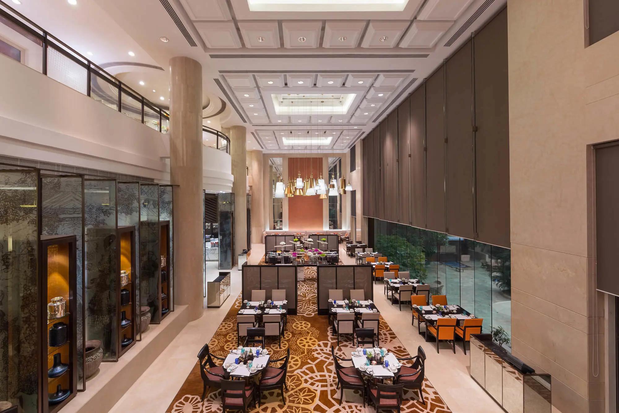 Modern dining area at Sheraton New Delhi, featuring high ceilings, elegant lighting, large windows, and neatly arranged tables in a spacious setting