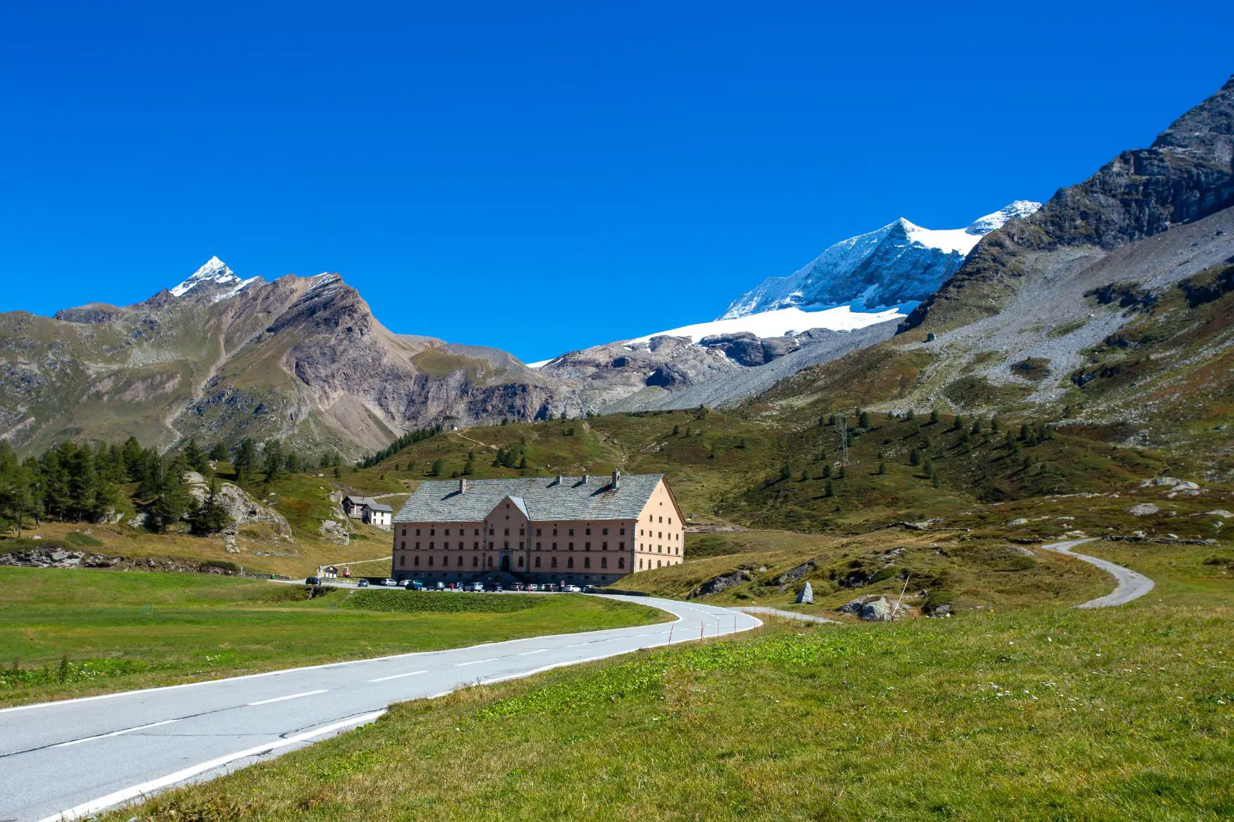 Simplon Pass in Switzerland, featuring the historic Simplon Hospice at the centre, surrounded by snow-covered alpine peaks and rugged mountain scenery