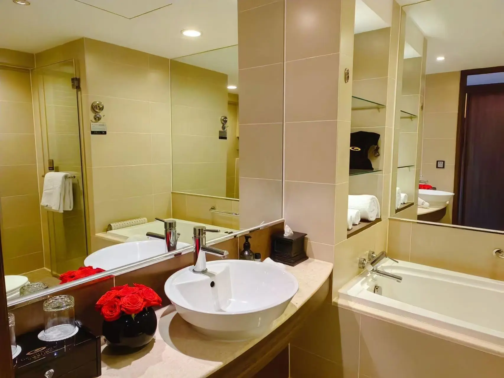A brightly lit bathroom showing a bath tub and shower in the mirror reflection, with a basin in the centre of the room, at the Grand Noble Hotel Xi’an in Xi’an, China