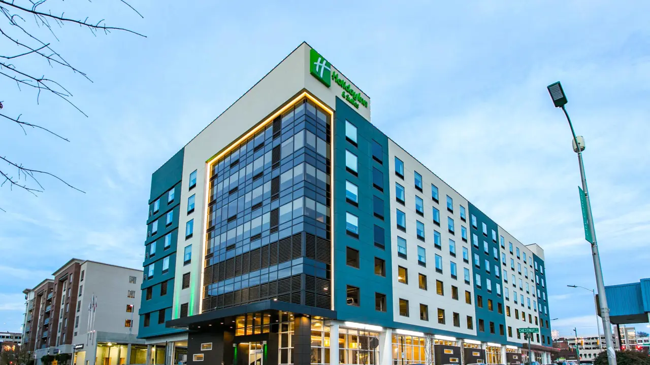 Exterior view of the Holiday Inn and Suites Downtown, Chattanooga, a modern multi-story hotel with large windows and a bright entrance, situated in an urban setting