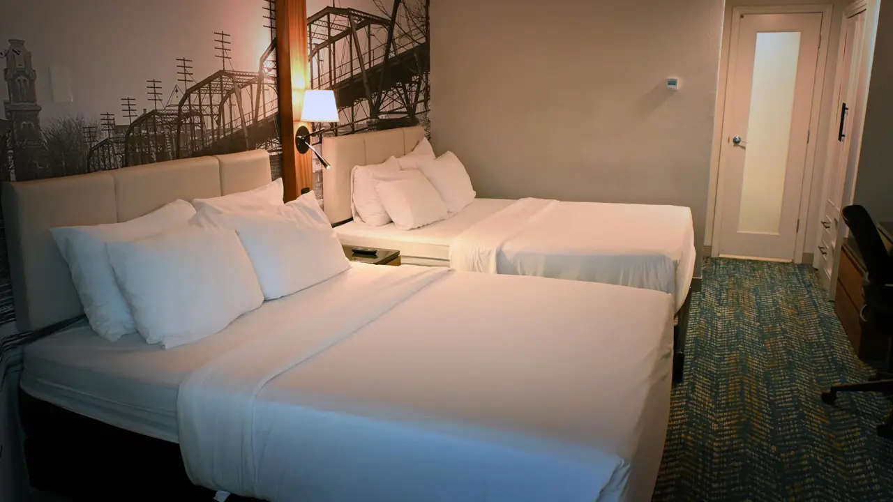 Double room at Fort Pontchartrain hotel, featuring two large beds with white linens, a monochrome mural of a historic bridge, bedside lighting, and a modern interior